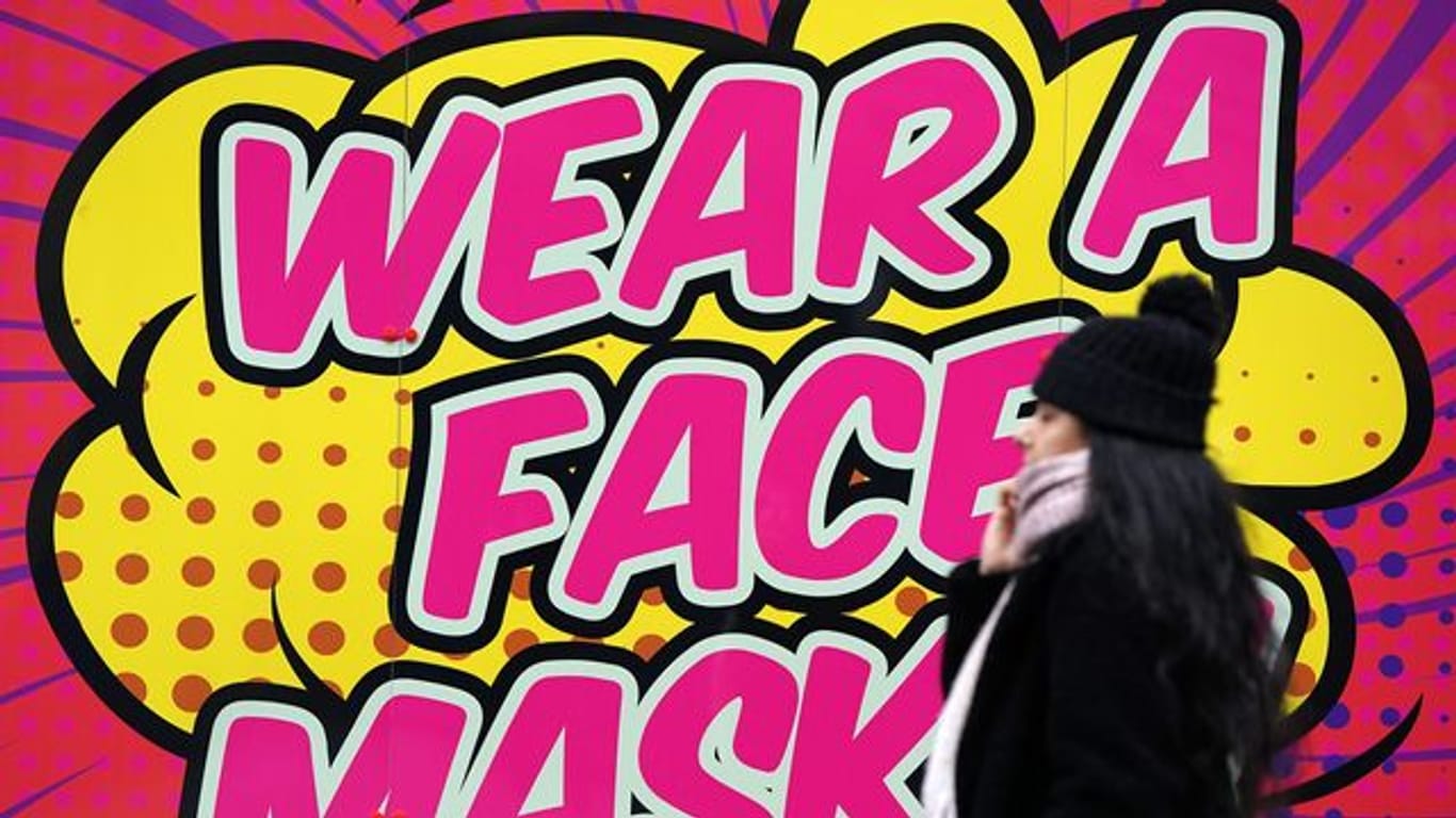 Eine Frau ohne Mund-Nasen-Schutz geht an einem farbigen Schild in Nottingham vorbei, das zum Tragen einer Mund-Nasen-Bedeckung auffordert.