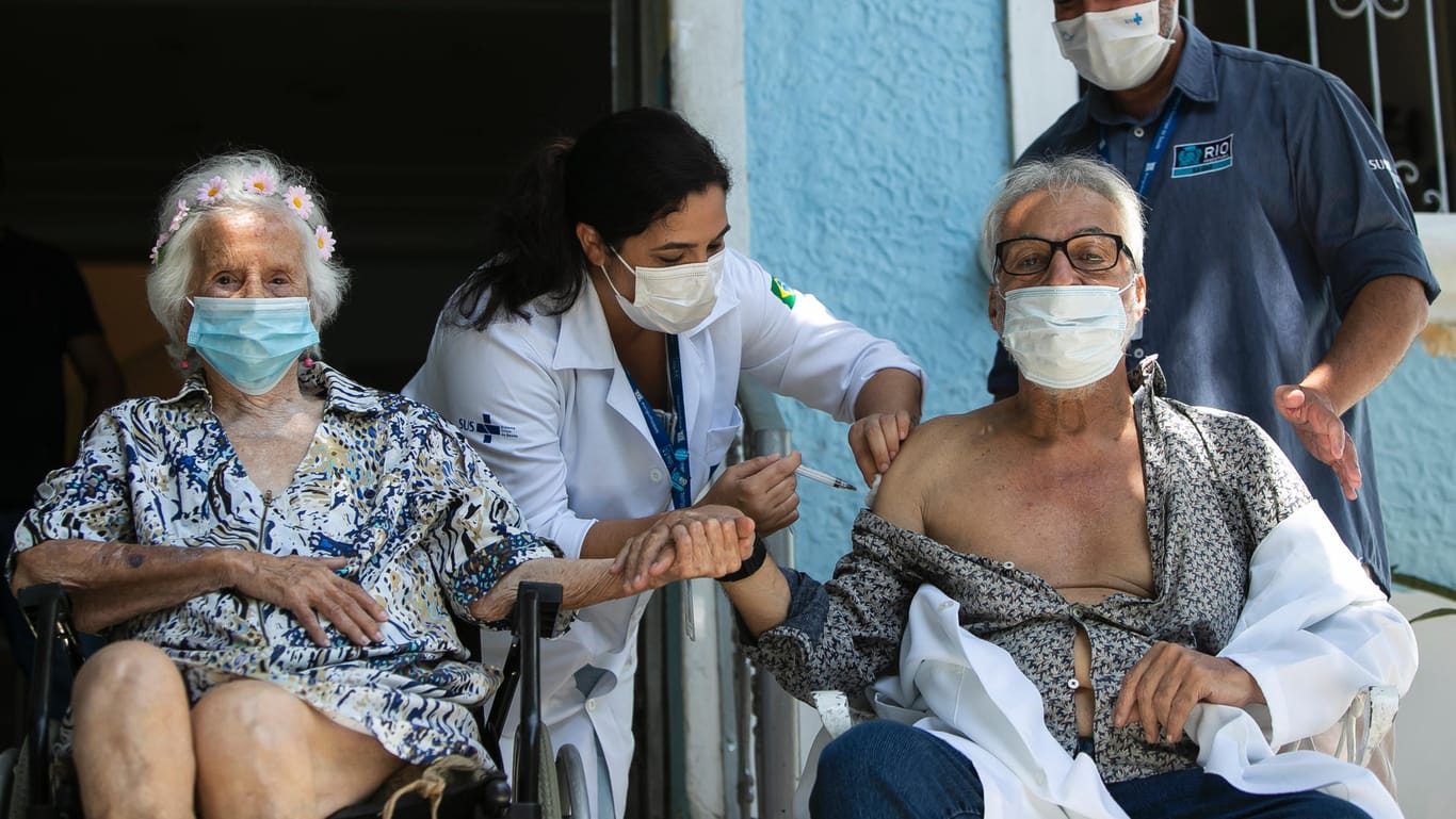 Brasilien, Rio De Janeiro: Die 106-jährige Zelia de Carvalho Morley (l) hält den 70-jährigen Paulo Cesar Cunha Fabiano (r) die Hand, während er eine Spritze mit dem chinesischen Sinovac CoronaVac-Impfstoff im Altersheim erhält.