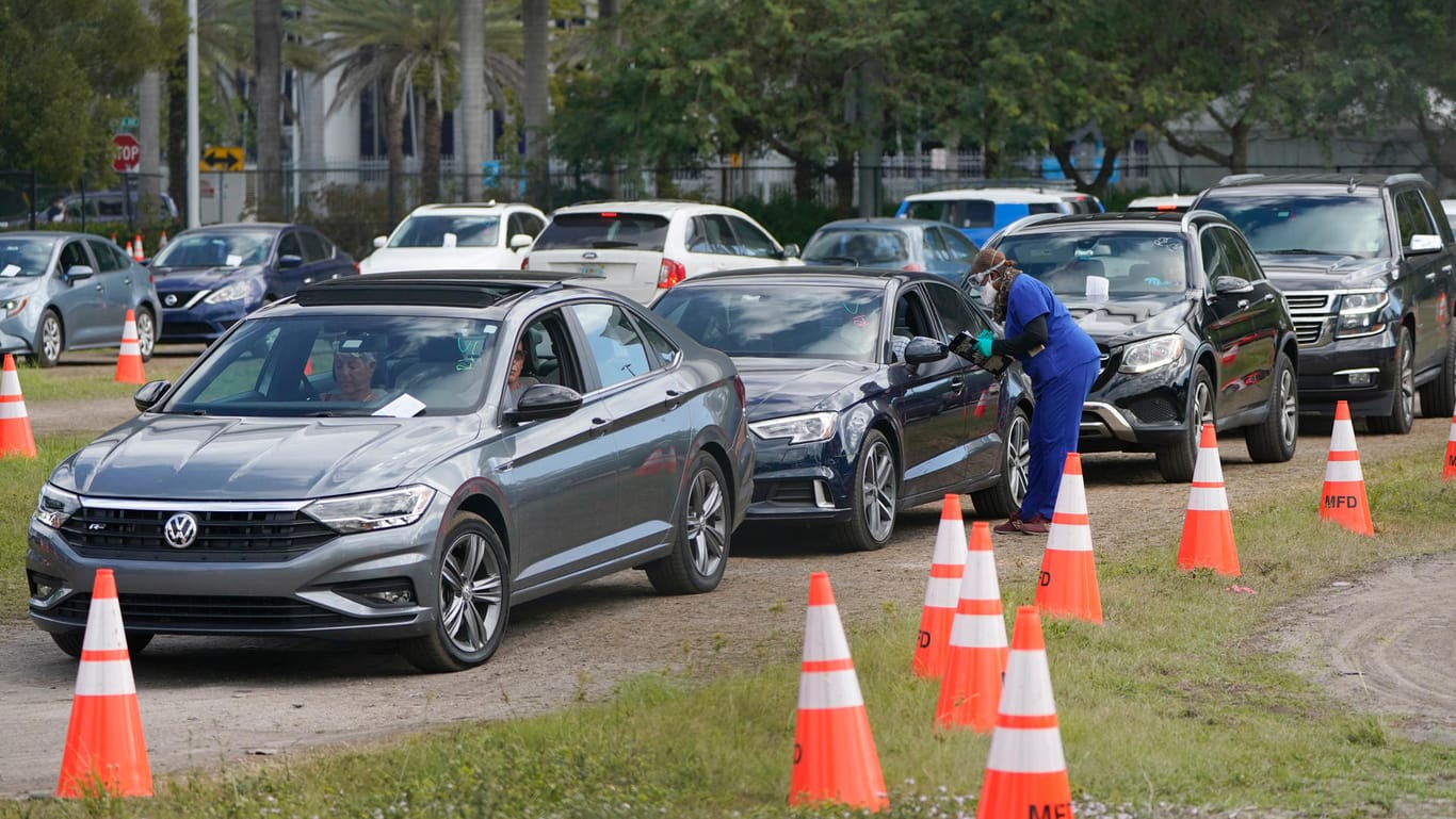 USA, Miami: Eine Mitarbeiterin des Gesundheitswesens spricht mit einem Autofahrer, der mit seinem Auto in der Schlange eines Drive-In Corona-Impfzentrums am Marlins Park steht.
