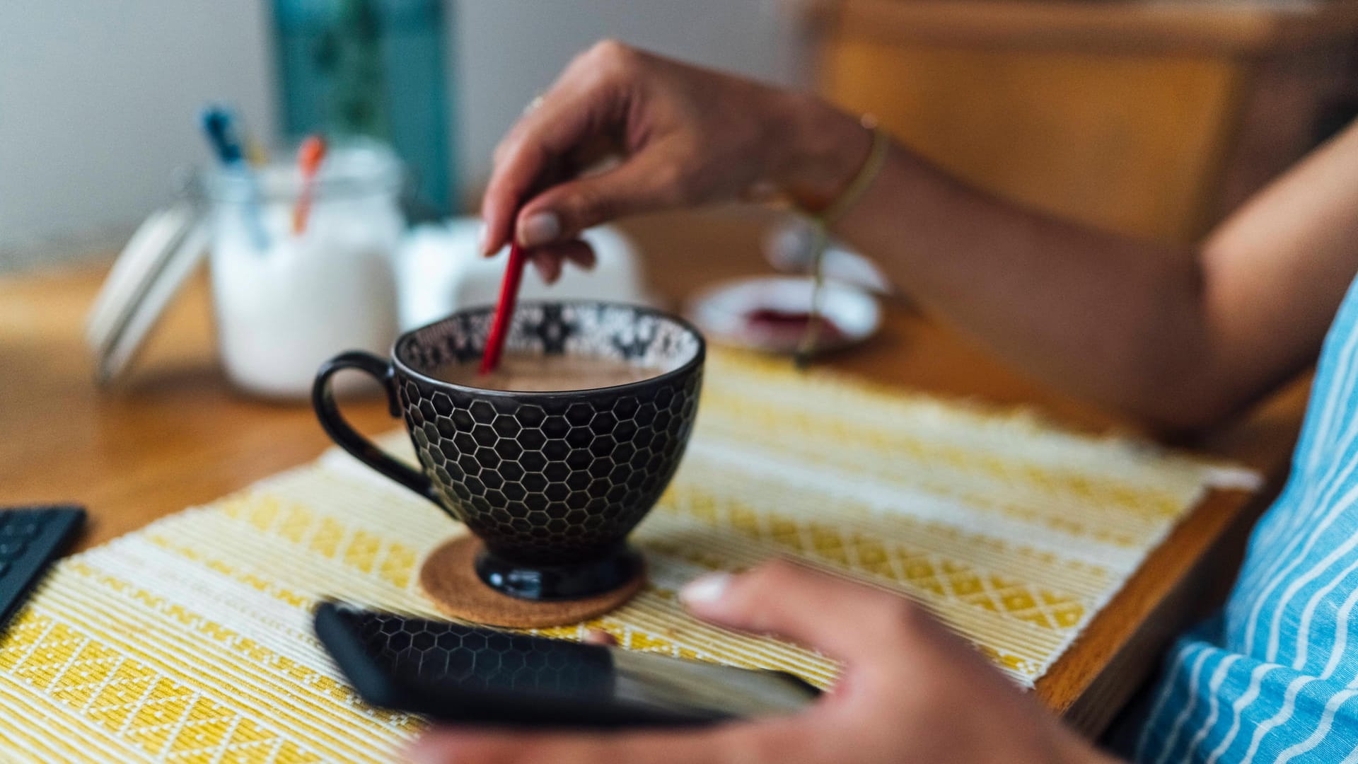 Eine Frau hält ein Telefon in der Hand und rührt im Kaffee (Symbolbild). Erneut ist eine Frau Opfer des Enkeltricks geworden, bei dem die Täter ältere Menschen anrufen und um Geld bitten.