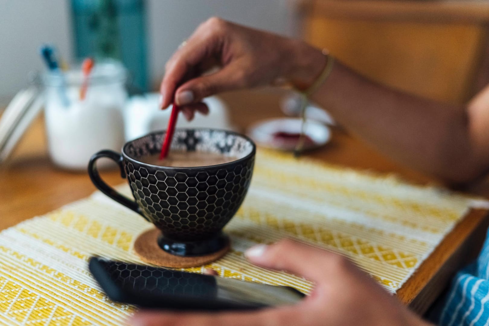 Eine Frau hält ein Telefon in der Hand und rührt im Kaffee (Symbolbild). Erneut ist eine Frau Opfer des Enkeltricks geworden, bei dem die Täter ältere Menschen anrufen und um Geld bitten.