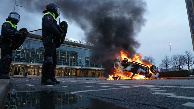 Flammen schlagen aus einem Auto, das vor dem Bahnhof in Eindhoven auf dem Kopf liegt.