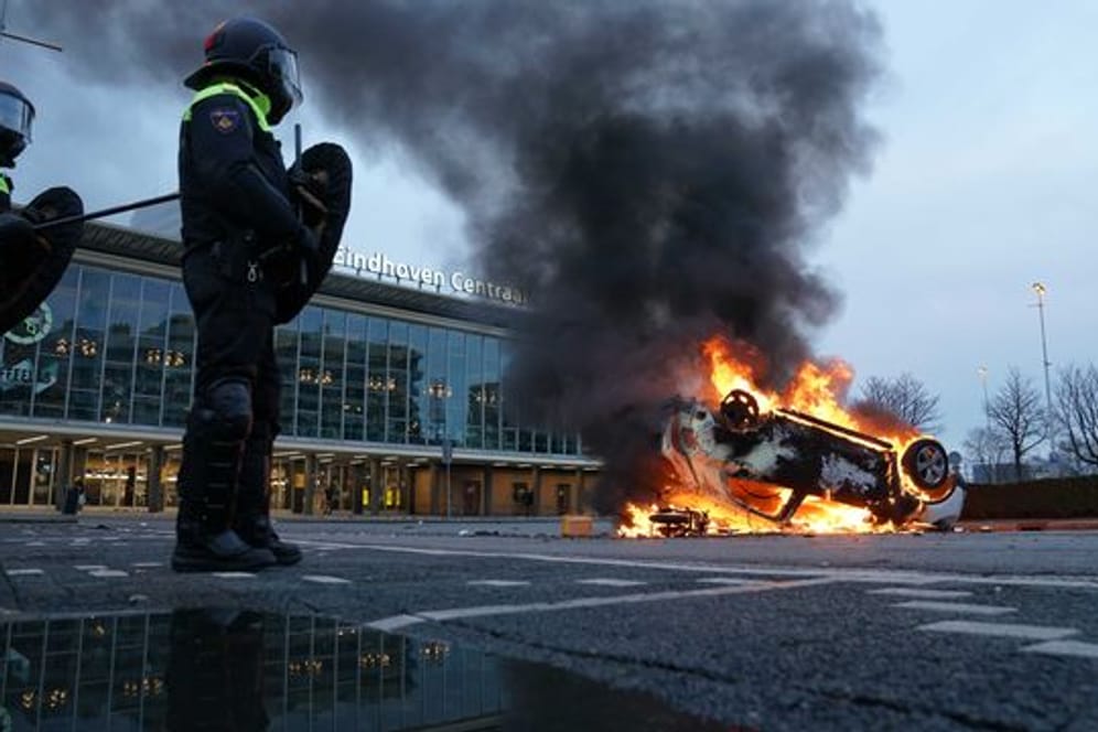 Flammen schlagen aus einem Auto, das vor dem Bahnhof in Eindhoven auf dem Kopf liegt.