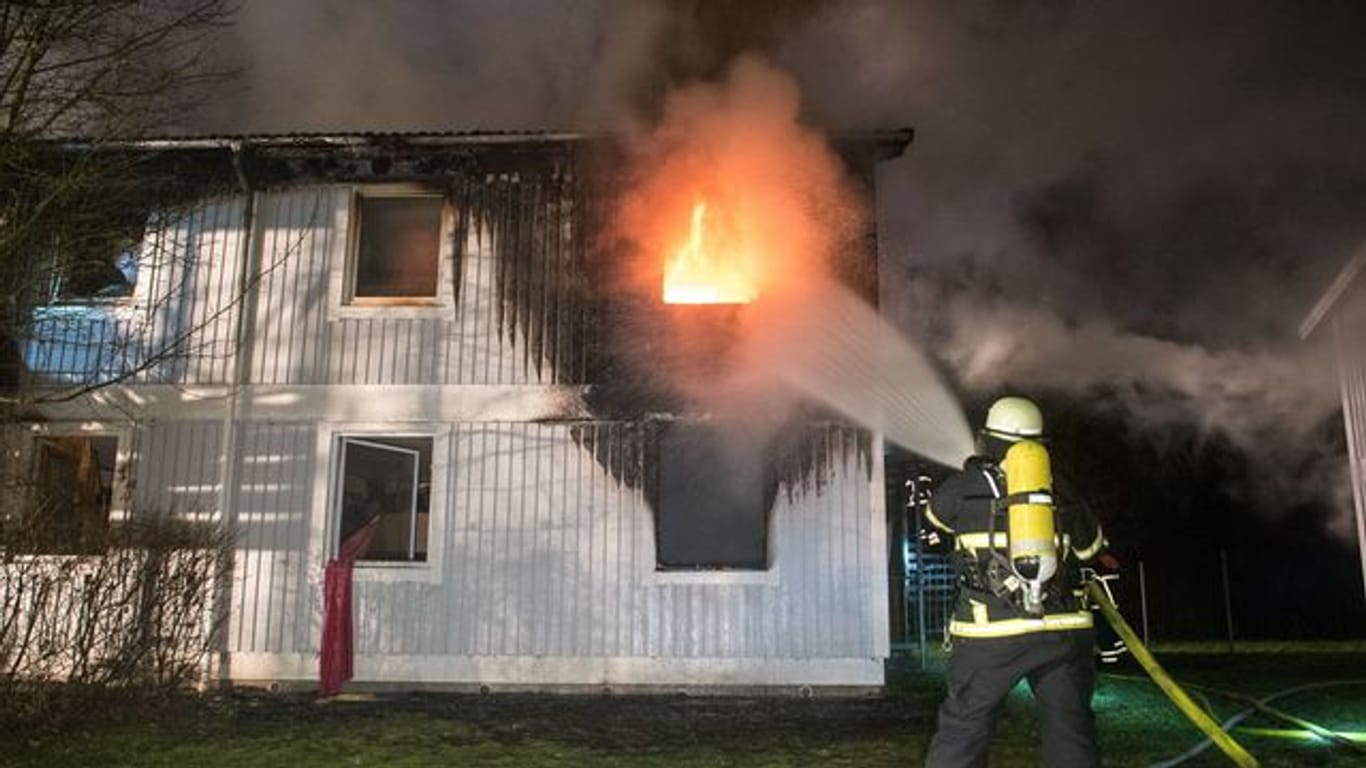Flammen schlagen aus einem Fenster: Ein Mitarbeiter der Feuerwehr löscht einen Brand in einer Unterkunft für Flüchtlinge.