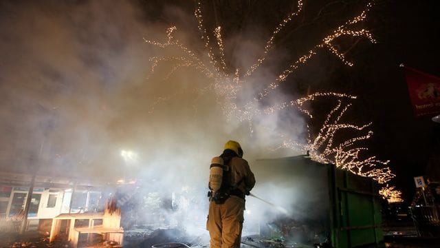 Krawalle in Rotterdam: Ein Feuerwehrmann löscht einen Container, der bei Protesten gegen die landesweite Ausgangssperre in Brand gesetzt wurde. Krawalle in Rotterdam: Ein Feuerwehrmann löscht einen Container, der bei Protesten gegen die landesweite Ausgangssperre in Brand gesetzt wurde.