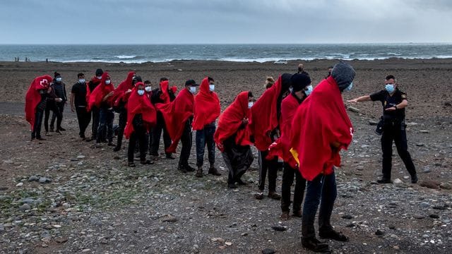 Migranten aus Marokko stehen an einem Strand auf Gran Canaria, nachdem sie den Atlantik mit einem Holzboot überquert haben.
