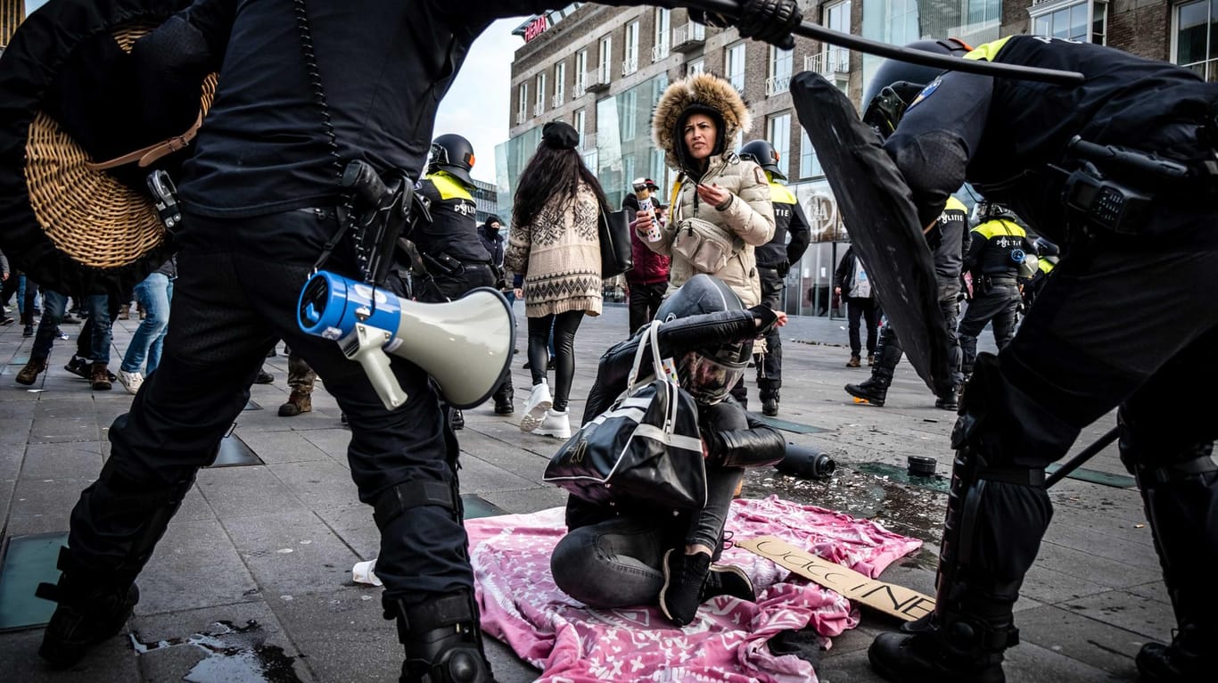 Eindhoven: Zwei Polizisten beugen sich über eine Demonstrantin, die auf einer Straße sitzt. Mehrere hundert Menschen haben vor dem Bahnhof gegen die aktuelle Corona-Politik demonstriert.