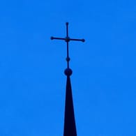 Ein Kreuz ist auf einer Kirchturmspitze zu sehen (Symbolbild): Viele Kölner sind enttäuscht von der Kirche und ziehen ihre Konsequenzen.