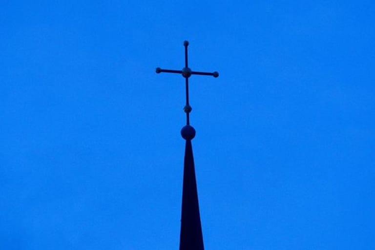 Ein Kreuz ist auf einer Kirchturmspitze zu sehen (Symbolbild): Viele Kölner sind enttäuscht von der Kirche und ziehen ihre Konsequenzen.