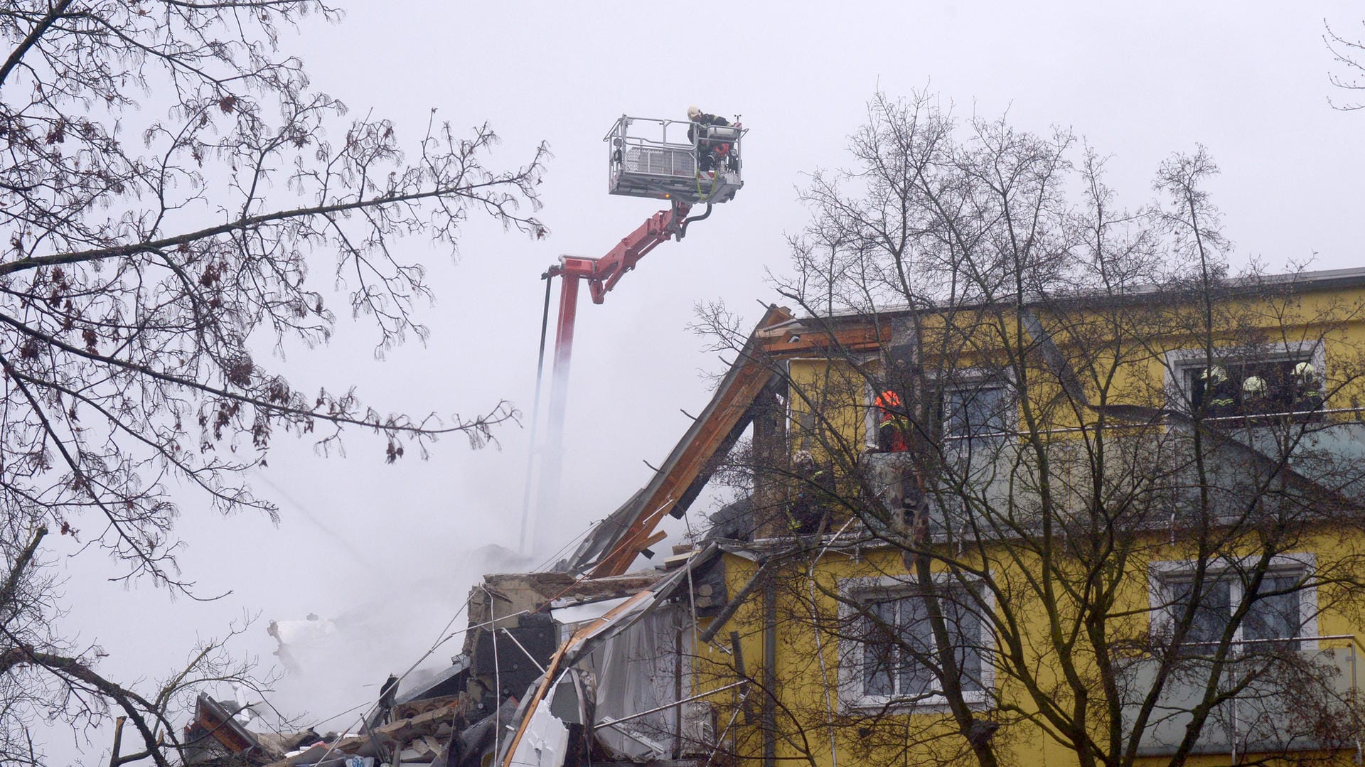 Feuerwehrleute stehen während Löscharbeiten nach einer Explosion auf der Leiter eines Löschzugs.