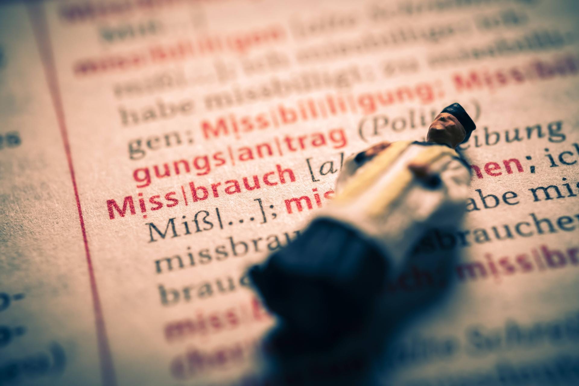 Miniaturfigur eines Priesters in einem Wörterbuch mit dem Wort Missbrauch: In Berlin ist ein Gutachten zum Missbrauch in der Kirche vorgestellt worden.