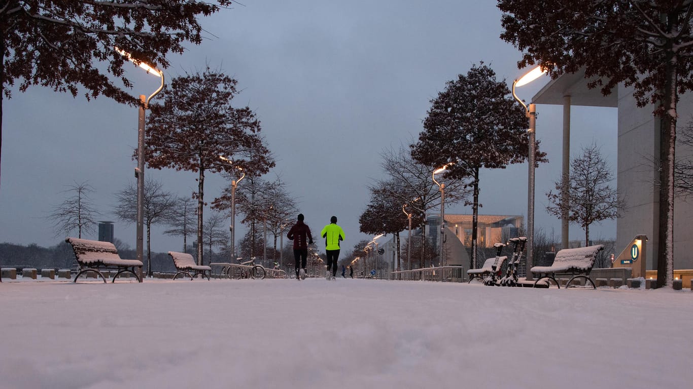 Zwei Jogger laufen am Morgen im Regierungsviertel über einen mit Schnee bedeckten Weg: Der Schnee bliebt über Nacht liegen.