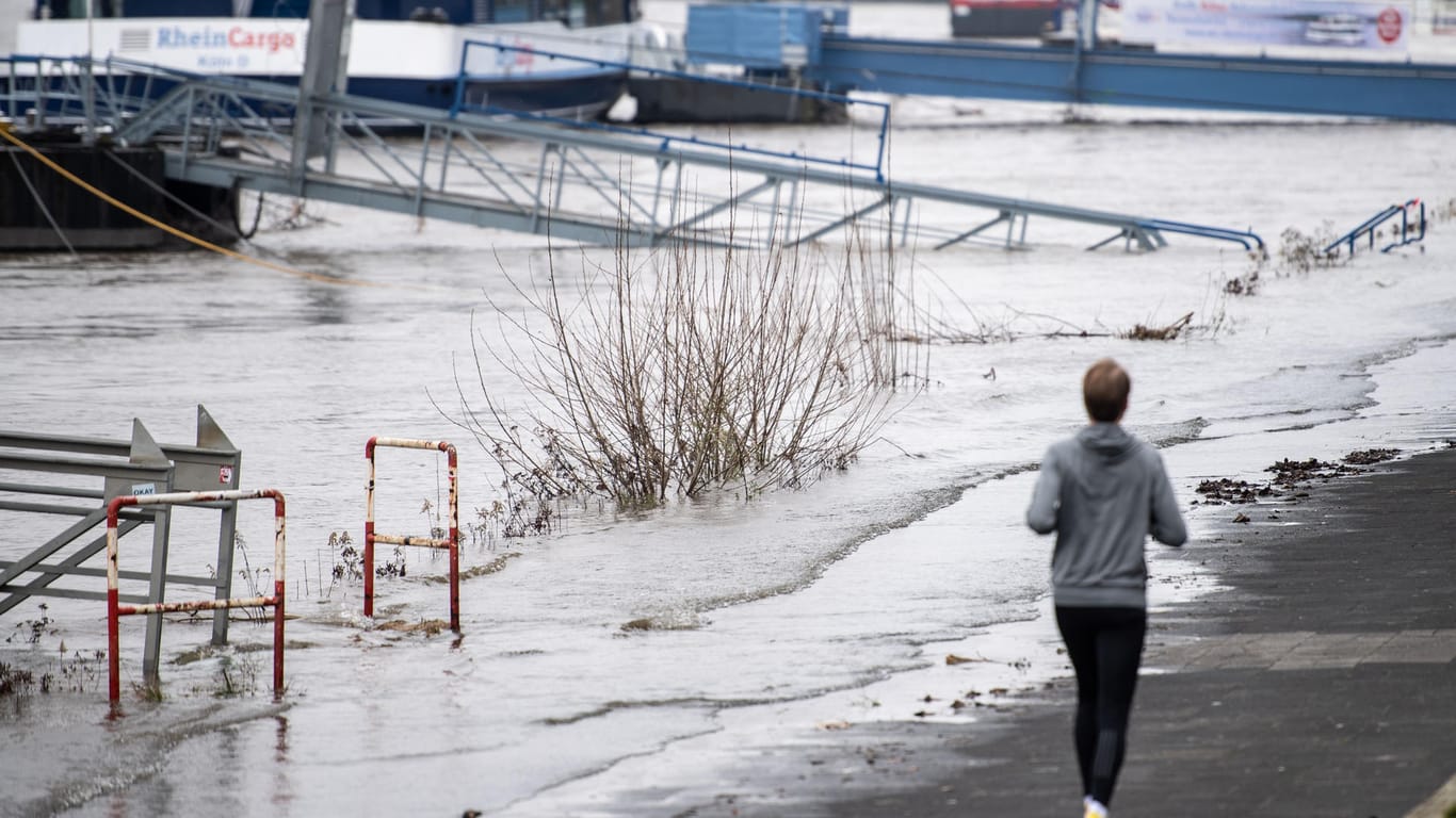 Ein Mann läuft am Rhein entlang, der über einen Weg am Ufer schwappt.