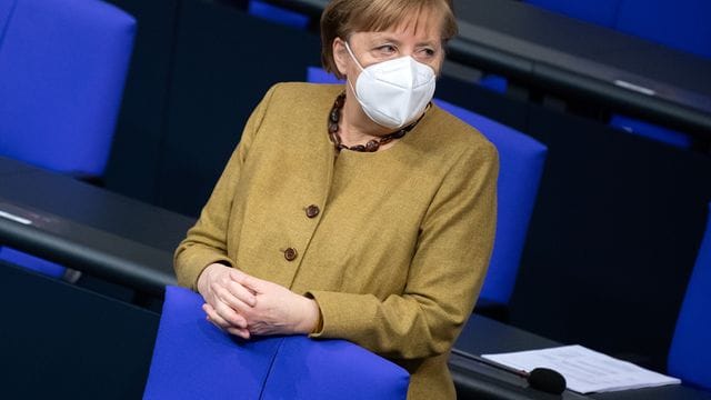 Bundeskanzlerin Angela Merkel (CDU) steht zu Beginn einer Plenarsitzung im Bundestag mit Schutzmaske an ihrem Platz.