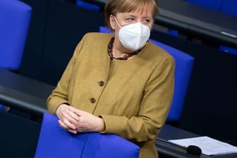 Bundeskanzlerin Angela Merkel (CDU) steht zu Beginn einer Plenarsitzung im Bundestag mit Schutzmaske an ihrem Platz.