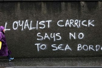 Eine Passantin geht in Belfast an einem Graffiti mit dem Schriftzug "Loyalist Carrick says no to Sea Border" (Loyalist Carrick sagt Nein zur Seegrenze) vorbei.