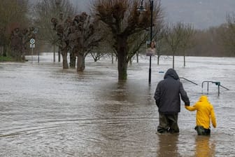 HochwasserZwei Menschen in Wathosen laufen über einen überfluteten Weg (Archivbild): In Rheinland-Pfalz hält das Hochwasser weiter an.