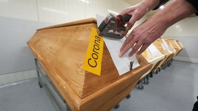 Ein Mitarbeiter eines Krematoriums in Rheinland-Pfalz bringt an einem Sarg die Markierung "Corona" an. Ein Mitarbeiter eines Krematoriums in Rheinland-Pfalz bringt an einem Sarg die Markierung "Corona" an.