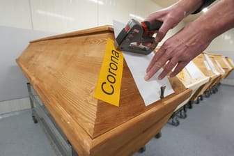Ein Mitarbeiter eines Krematoriums in Rheinland-Pfalz bringt an einem Sarg die Markierung "Corona" an.