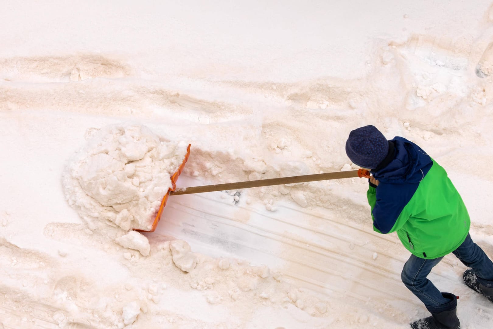 Eine Person schippt Schnee: Wegen des Saharastaubes ist er rötlich eingefärbt.