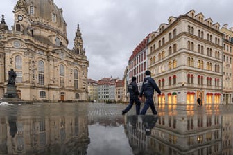 Dresden: Die Frauenkirche und die Häuser auf dem Neumarkt spiegeln sich am Nachmittag in einer nassen Steinbank während zwei Mitarbeiter der Polizeibehörde (Ordnungsamt) entlang laufen.