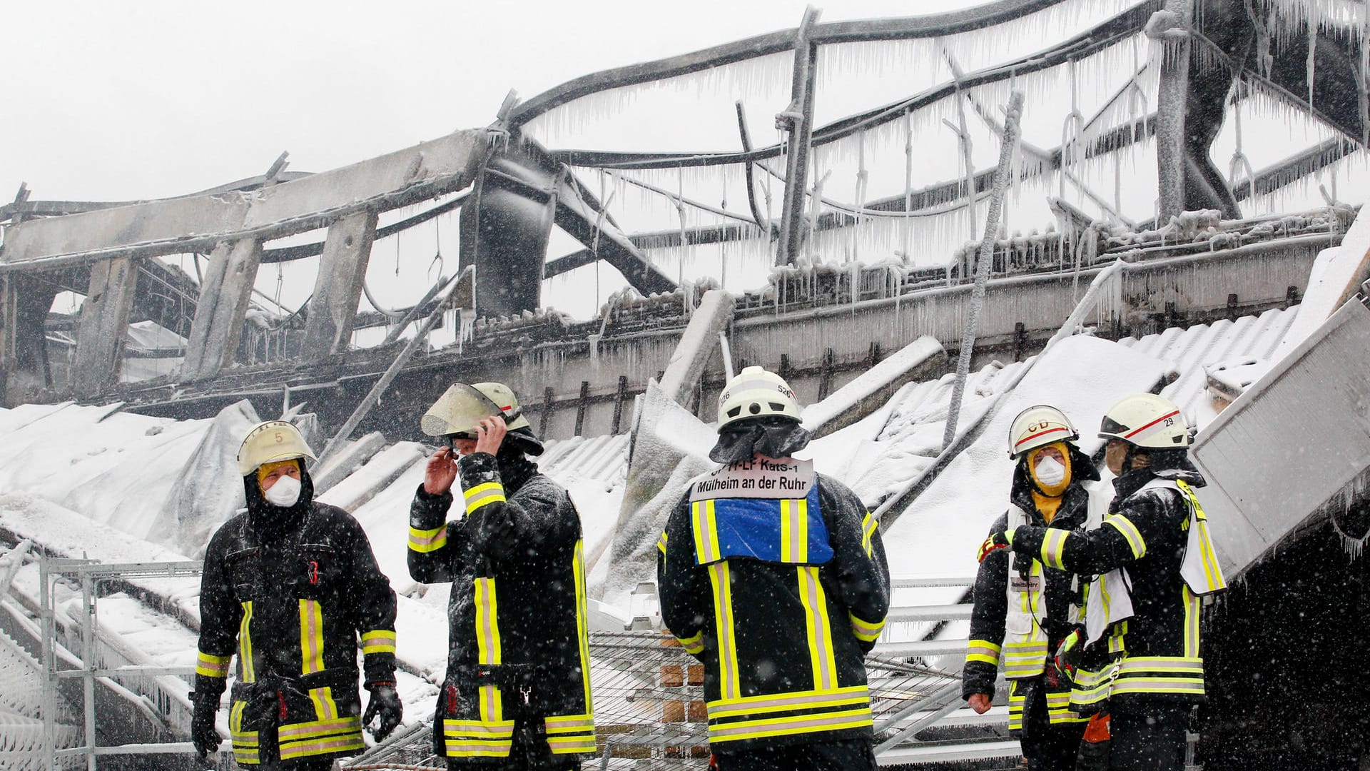 Feuerwehrmänner stehen vor der eingestürzten Halle: Wegen der eisigen Kälte ist das Löschwasser gefroren.