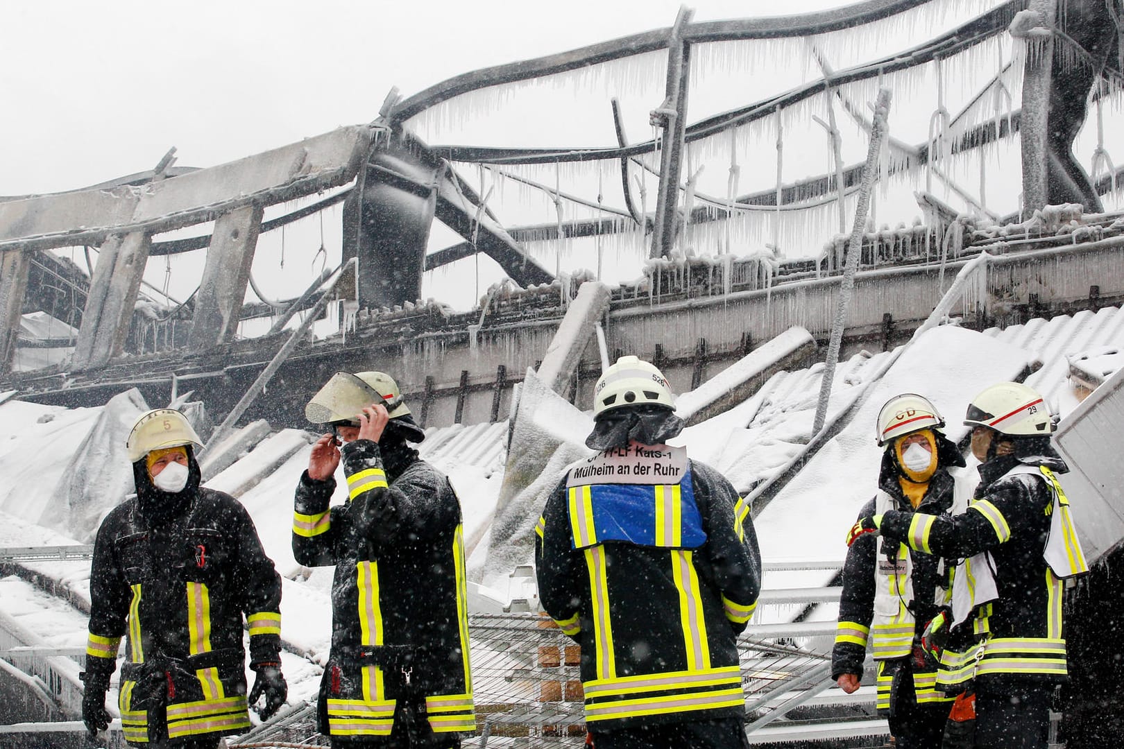 Feuerwehrmänner stehen vor der eingestürzten Halle: Wegen der eisigen Kälte ist das Löschwasser gefroren.