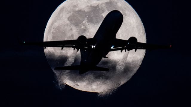 Eine Passagiermaschine startet auf dem Flughafen Frankfurt vor dem tief am Himmel stehenden "Supermond".