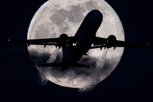 Eine Passagiermaschine startet auf dem Flughafen Frankfurt vor dem tief am Himmel stehenden "Supermond".