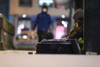 Ein Obdachloser sitzt am Abend in der Frankfurter Innenstadt mit seinem Hab und Gut vor einem geschlossenen Laden.: Angesichts von Schnee und Kälte ist die Situation wohnungsloser Menschen gefährlich.