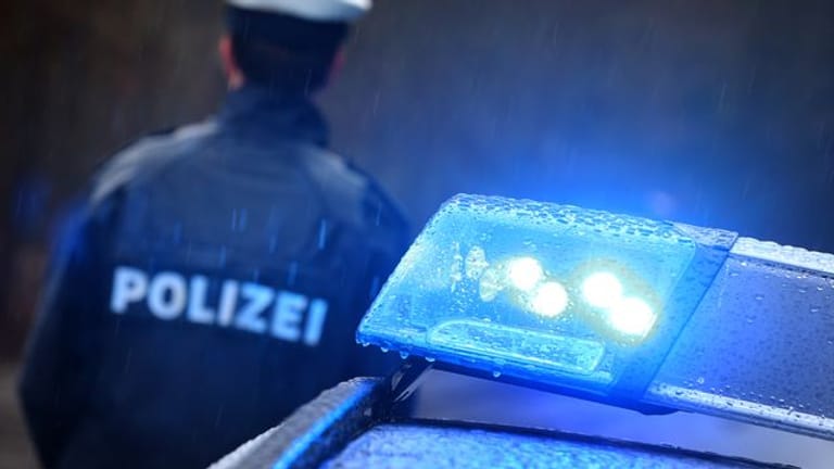 Ein Polizist steht im Regen vor einem Streifenwagen dessen Blaulicht aktiviert ist (Symbolbild): Wegen des Unfalls eines Sattelschleppers musste die A7 gesperrt werden.