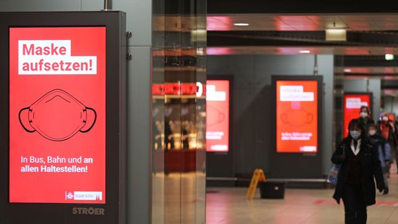 Der Schriftzug "Maske aufsetzten" steht im Kölner Hauptbahnhof auf einem Display.