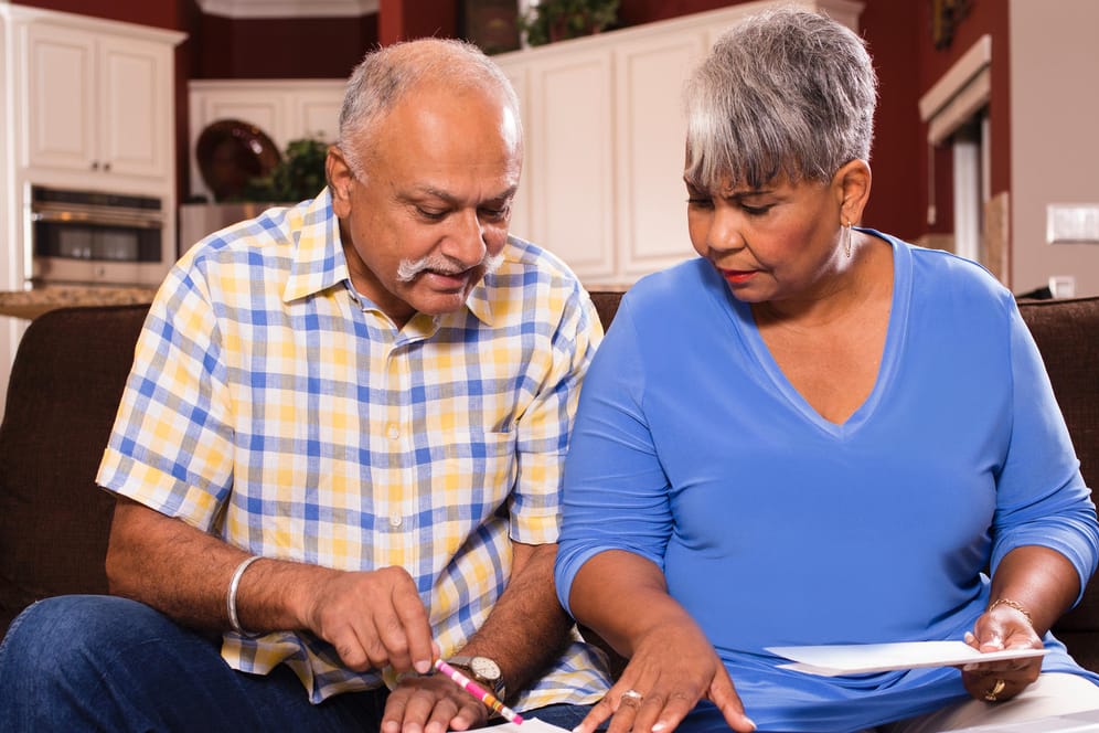 Älteres Ehepaar kniet über Unterlagen (Symbolbild): Wer nicht auf die gesetzliche Erbfolge setzen möchte, kann ein Testament schreiben.