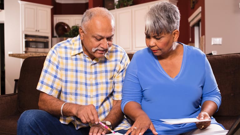 Älteres Ehepaar kniet über Unterlagen (Symbolbild): Wer nicht auf die gesetzliche Erbfolge setzen möchte, kann ein Testament schreiben.