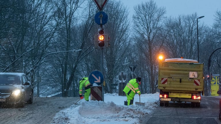 Zwei Mitarbeiter der Entsorgung Dortmund (EDG) befreien in der Morgendämmerung eine Verkehrsinsel vom Schnee: In der Stadt hat es stark geschneit.