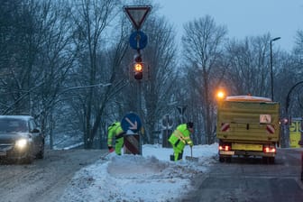 Zwei Mitarbeiter der Entsorgung Dortmund (EDG) befreien in der Morgendämmerung eine Verkehrsinsel vom Schnee: In der Stadt hat es stark geschneit.