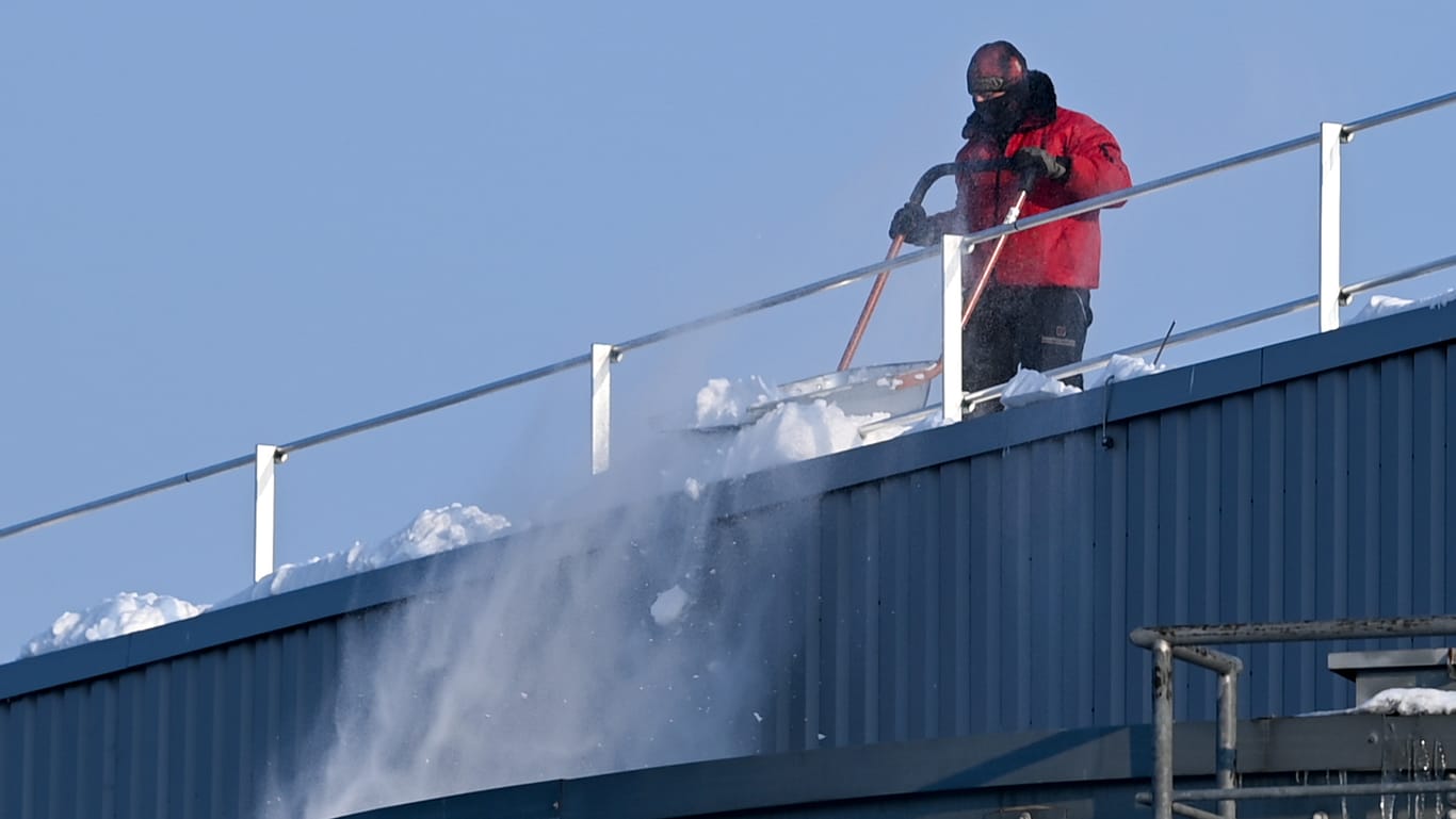 Eine Person schippt Schnee vom Dach des Lagers. Das Dach drohte unter der Schneelast einzubrechen.