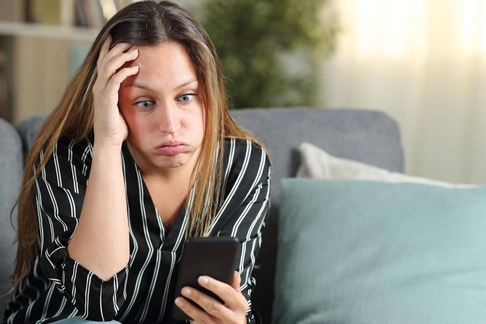 Eine Frau schaut frustriert auf ihr Handy (Symbolbild): Das LKA in Mainz warnt vor einer neuen Betrugsmasche via SMS.