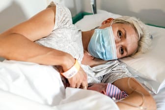 Eine Mutter stillt mit Mundschutz ihr Neugeborenes (Symbolbild): Die Pandemie fordert die Geburtshilfe und werdende Eltern heraus.