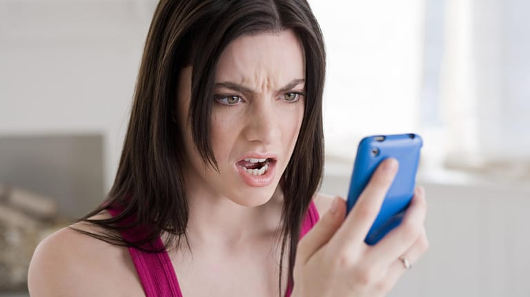 Eine Frau schaut wütend auf ihr Handy: Die Bundesnetzagentur hat einen Provider wegen unerlaubter Telefonwerbung zu einer Strafe verdonnert.