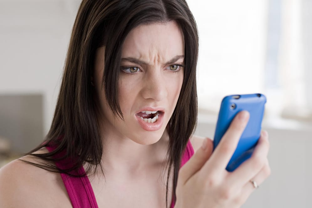 Eine Frau schaut wütend auf ihr Handy: Die Bundesnetzagentur hat einen Provider wegen unerlaubter Telefonwerbung zu einer Strafe verdonnert.