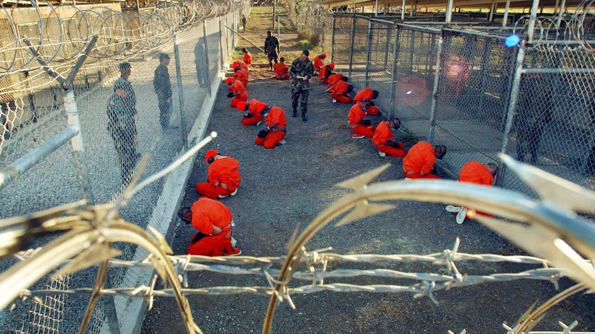 US-Gefangenlager Guantanamo: In orangefarbene Overalls gekleidete Häftlinge knien im Camp X-Ray, einem Teil des Lagers, auf dem Boden.