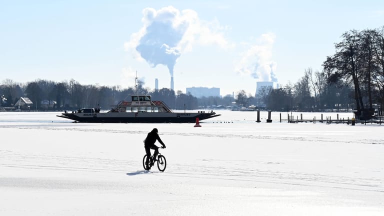 Die Havel ist zugefroren und die ersten Menschen wagen sich auf das Eis: Im Hintergrund ist die Autofähre nach Spandau zu sehen.