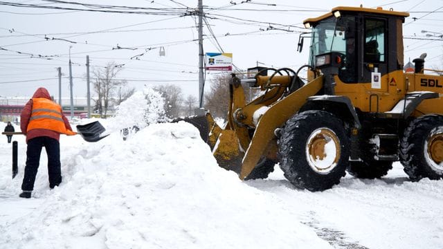 Schnee wegräumen mit schwerem Gerät: Ein Mann schippt Schnee in die Schaufel eines Baggers. Schnee wegräumen mit schwerem Gerät: Ein Mann schippt Schnee in die Schaufel eines Baggers.