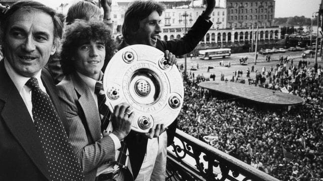 Kevin Keegan (M) feiert mit Meisterschale in Händen zwischen HSV-Trainer Branco Zebec (l) und Abwehrspieler Manfred Kaltz den Erfolg.