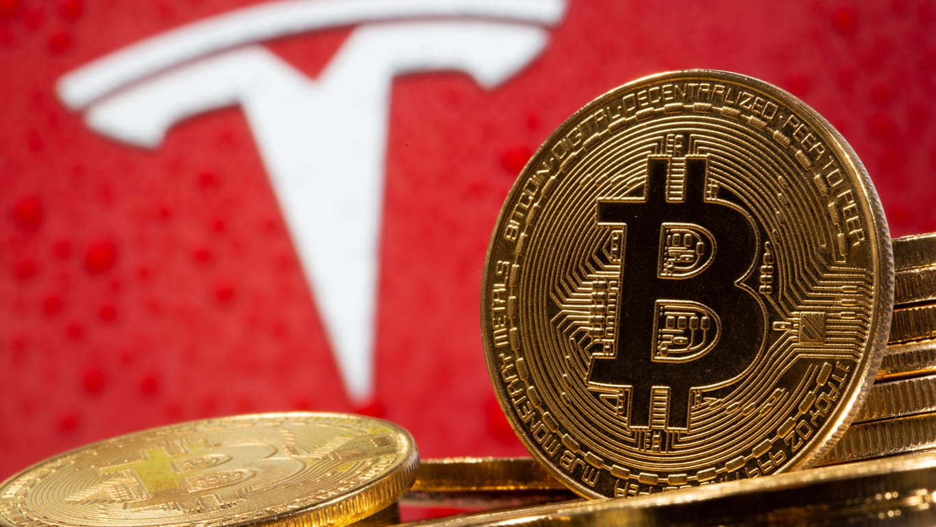 Ein Bitcoin vor dem Tesla-Logo (Symbolbild): Die Kryptowährung steigt seit der Ankündigung des E-Autobauers, in Bitcoin zu investieren.