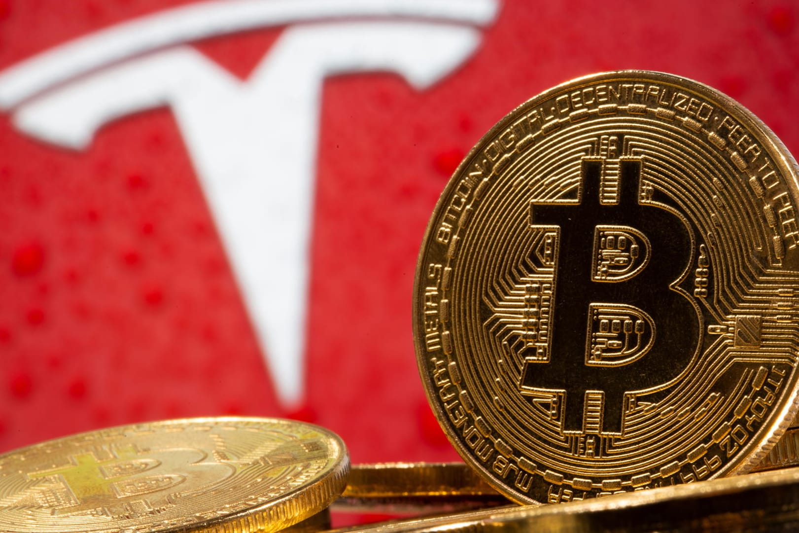 Ein Bitcoin vor dem Tesla-Logo (Symbolbild): Die Kryptowährung steigt seit der Ankündigung des E-Autobauers, in Bitcoin zu investieren.