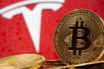 Ein Bitcoin vor dem Tesla-Logo (Symbolbild): Die Kryptowährung steigt seit der Ankündigung des E-Autobauers, in Bitcoin zu investieren.