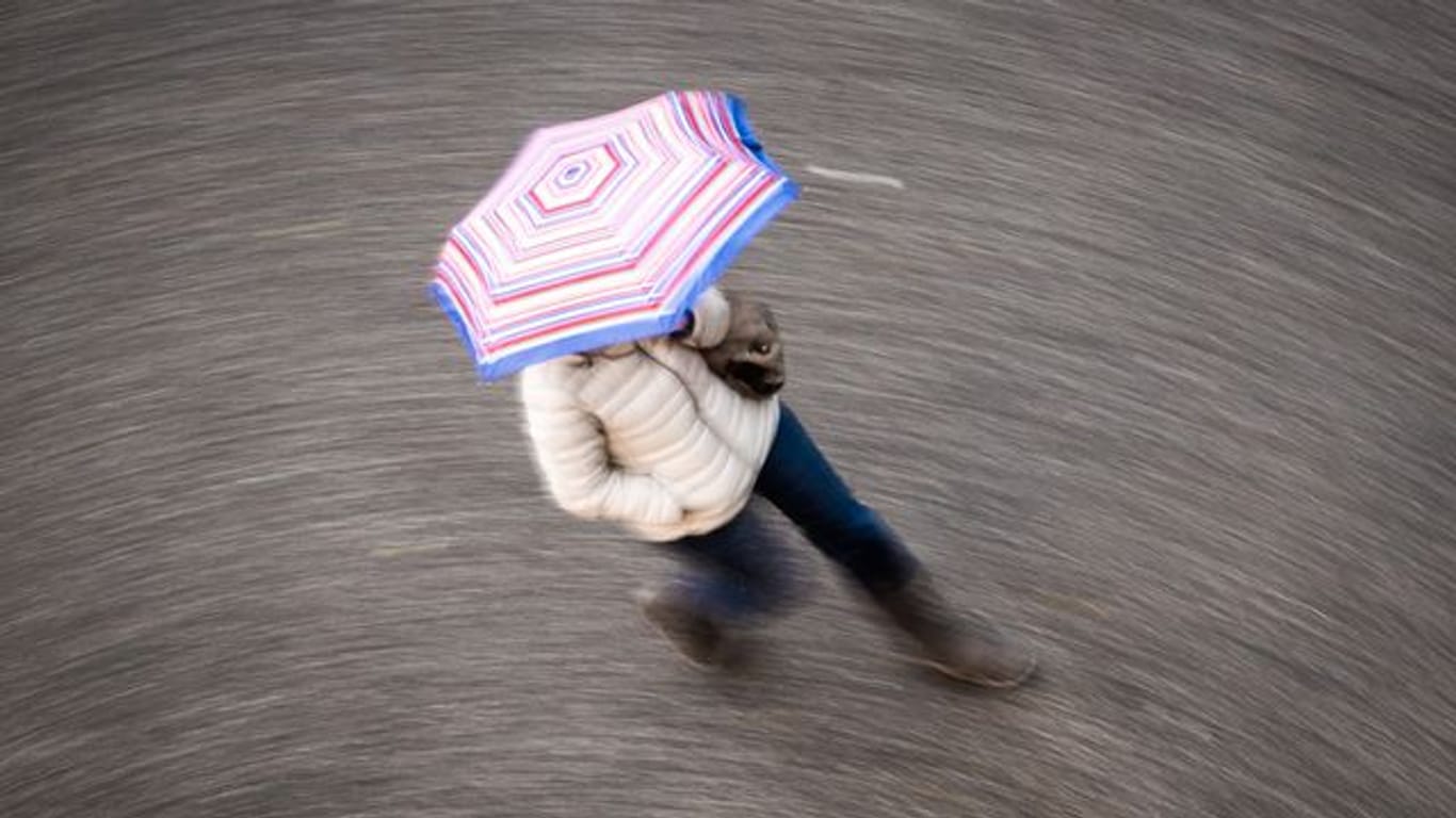 Eine Frau geht bei regnerischem Wetter über eine Straße (Symbolbild): Am Dienstag soll der Schnee in Berlin und Brandenburg von Regen abgelöst werden.