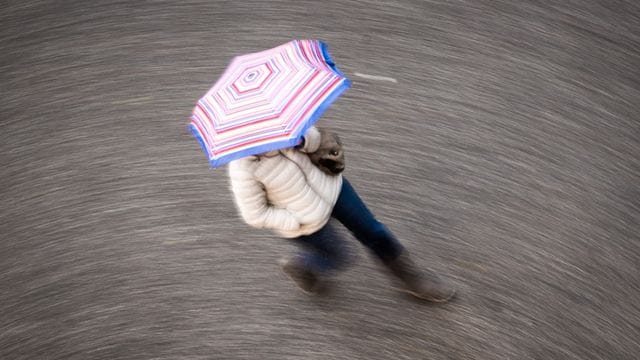 Eine Frau geht bei regnerischem Wetter über eine Straße (Symbolbild): Am Wochenende wird es an einem Tag deutlich frischer, auch die Nächte werden kalt.